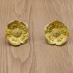 May include: A pair of gold-tone flower-shaped earrings with a textured surface.