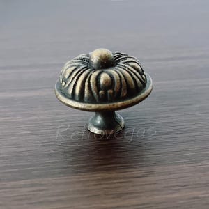 May include: An antique brass cabinet knob with a decorative floral design. The knob features a fluted top and a short pedestal base. The finish is a warm, aged brass colour, adding a vintage touch to furniture.