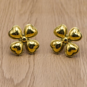 Op de afbeelding: Een paar gouden oorbellen in de vorm van vierbladige klavers. De oorbellen zijn gemaakt van metaal en hebben een glanzende afwerking.