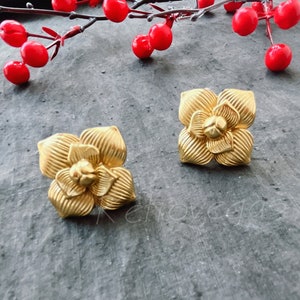 Könnte beinhalten: Ein Paar goldfarbene Ohrringe in Blumenform. Die Ohrringe sind aus Metall und haben eine strukturierte Oberfläche.