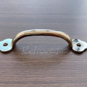 May include: Silver metal drawer pull with a rounded shape and flower-shaped ends.
