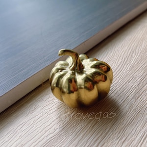 May include: A gold-coloured metal pumpkin figurine. The pumpkin has a smooth, shiny surface and a detailed stem.