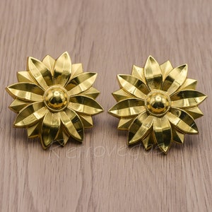 May include: A pair of gold-tone flower-shaped earrings. Each earring features a central round bead and multiple petals.