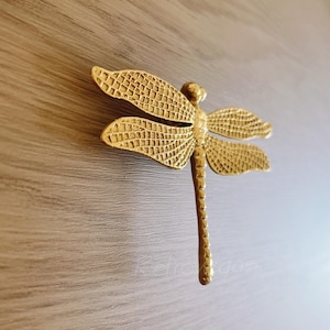 May include: A gold-toned dragonfly door handle with a textured surface.