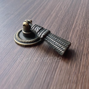 May include: A bronze cabinet knob with a rope-like design and a round base. The knob has a dark brown finish and a textured surface.