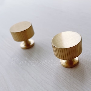 May include: Two gold-toned cabinet knobs with a ribbed design. The knobs are round and have a small base.