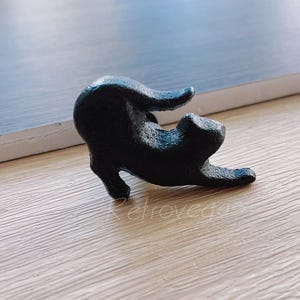 Peut inclure: Une figurine de chat en céramique noire en position recroquevillée. Le chat est posé comme s'il s'étirait ou bâillait.
