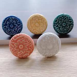 May include: Five ceramic knobs with floral designs in various colours, including blue, yellow, white, and orange.