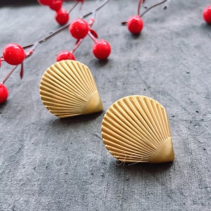 May include: A pair of gold-tone earrings shaped like seashells. The earrings have a fan-like design and are a classic style.
