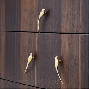 May include: Three gold bird-shaped drawer pulls on a dark wood cabinet.