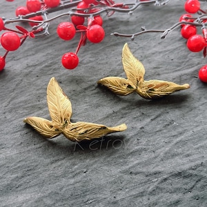 Könnte beinhalten: Zwei goldene Ohrringe in Blattform mit einem filigranen Design. Die Ohrringe liegen auf einer grauen, strukturierten Oberfläche.