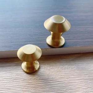 May include: Two gold-toned cabinet knobs with a rounded, slightly domed top. The knobs are made of metal and have a smooth, polished finish.