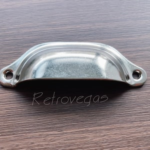 May include: A silver metal drawer pull with a curved, rounded shape. The pull has a smooth, polished finish.