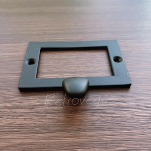 May include: Black metal rectangular plate with a rounded edge and a single black knob in the centre. The plate has a rectangular cutout in the centre.
