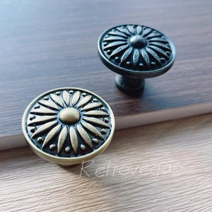 May include: Two decorative cabinet knobs with a floral design. One knob is gold with a black center and the other is black with a silver center.