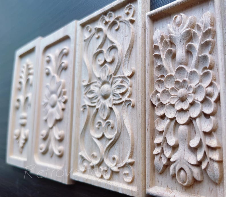 May include: Four rectangular wooden panels with intricate floral and scrollwork carvings. The panels are light-colored, possibly unfinished, and arranged in a row, showcasing detailed relief patterns. The carvings include flowers, leaves, and swirling designs.