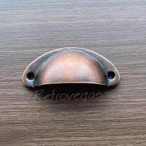 May include: A copper-toned cup-shaped drawer pull with a rounded top and two small holes on the sides.