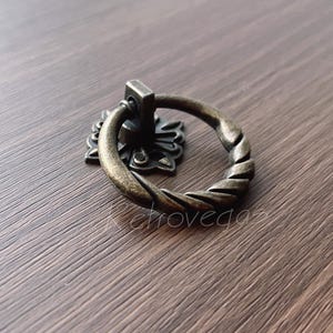 以下が含まれることがあります： ねじれたロープのデザインが施された、装飾的で華やかなブロンズ色のリングプルハンドル。キャビネット、引き出し、ドアに適しています。