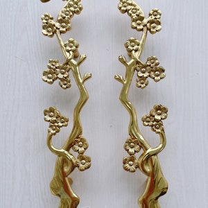 Peut inclure: Une paire de poignées de porte dorées avec un motif floral. Les poignées sont en forme de branche d'arbre avec des fleurs.