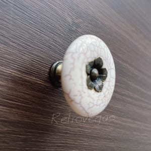 May include: White ceramic cabinet knob with a crackled finish and a bronze flower design.