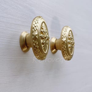 May include: Two gold oval-shaped cabinet knobs with a decorative floral design.
