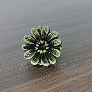 May include: A bronze-colored, flower-shaped cabinet knob. The knob has detailed petals and a dark center, giving it a vintage look. The hardware is designed for furniture and home decor projects.