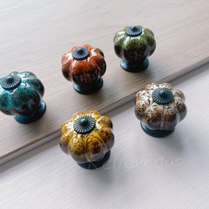 Puede incluir: Cinco pomos de cajón de cerámica con forma de calabaza con esmaltes de diferentes colores. Los pomos tienen un acento de metal negro en el centro.