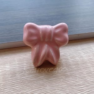 May include: A pink ceramic bow-shaped cabinet knob or drawer pull.