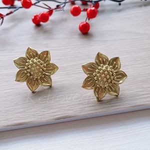 Op de afbeelding: Een paar gouden zonnebloem oorbellen. De oorbellen zijn gemaakt van metaal en hebben een gedetailleerd ontwerp.