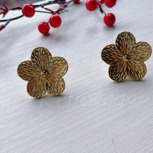 May include: A pair of gold flower-shaped earrings. The earrings have a textured surface and a small, round centre.