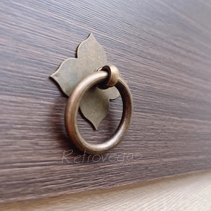 May include: A brass drawer pull with a decorative flower design and a ring handle.