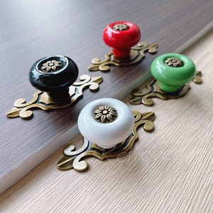 May include: Four ceramic cabinet knobs with ornate gold metal bases. The knobs are in black, white, red, and green.