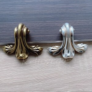 May include: Two decorative drawer pulls, one gold and one silver, with a floral design.