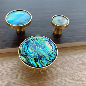 May include: Three brass cabinet knobs with iridescent abalone shell inlays. The knobs are round and have a smooth, polished finish. The abalone shell inlays feature a variety of colours, including blue, green, and gold.