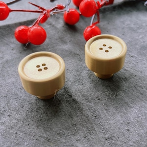 May include: Two wooden knobs with a button design. The knobs are light brown and have four holes in the center of the button.