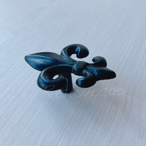 May include: Black metal fleur-de-lis cabinet knob with intricate details.