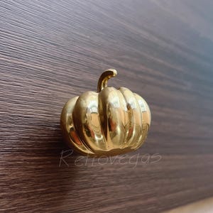 Puede incluir: Una perilla de gabinete o tirador de cajón en forma de calabaza de color dorado.