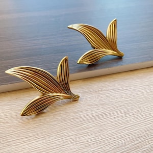 May include: Two gold leaf-shaped drawer pulls with a textured finish. The pulls are made of metal and have a delicate, elegant design.