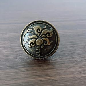 May include: Antique brass-toned cabinet knob with an ornate floral design. The round knob features a raised pattern of swirling leaves and a central flower. A decorative hardware piece for furniture.