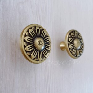 May include: Two gold-toned metal cabinet knobs with a floral design. The knobs have a round base and a raised floral pattern.