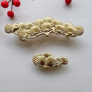 May include: Two gold-toned metal drawer pulls shaped like stylized pine branches with fan-shaped leaves.