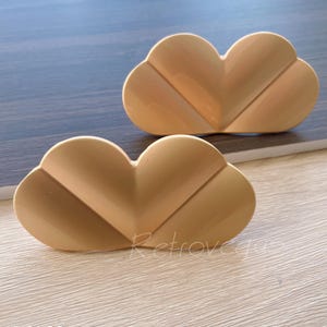 May include: Two gold-colored, heart-shaped cabinet knobs with a decorative, geometric design.