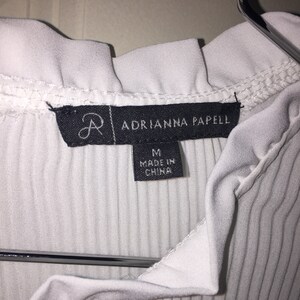 May include: White ribbed top with a ruffled neckline and a black tag that reads "Adrianna Papell" and "M Made in China".