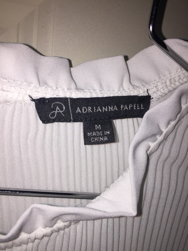 May include: White ribbed top with a ruffled neckline and a black tag that reads "Adrianna Papell" and "M Made in China".