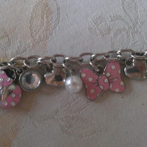 Puede incluir: Pulsera de abalorios plateada con varios abalorios, incluyendo un lazo rosa con lunares blancos, una mariquita, una perla, corazones y un bolso rosa. La pulsera tambi&eacute;n presenta abalorios transparentes, redondos y en forma de l&aacute;grima.