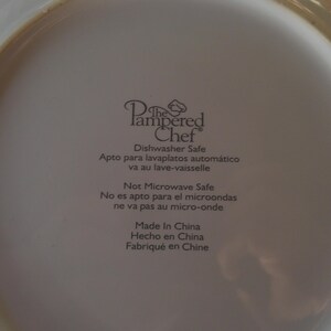 May include: Close-up of the back of a white plate with the text "The Pampered Chef" and other text indicating it is dishwasher safe and made in China.