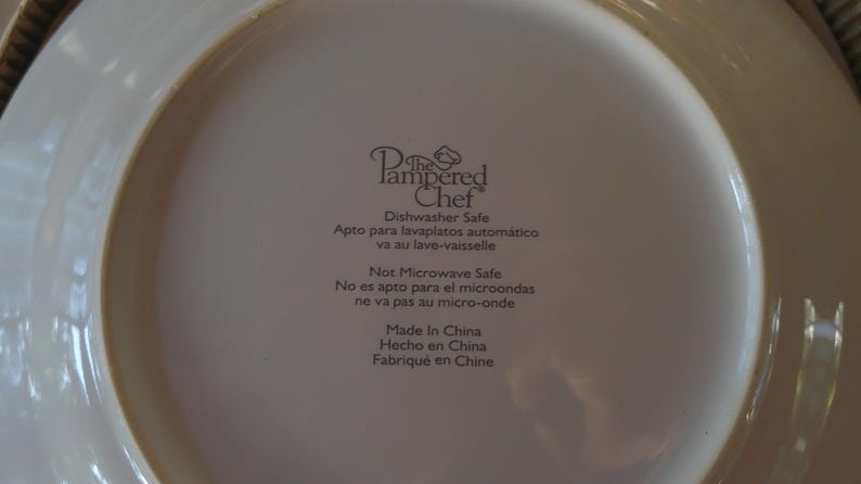 May include: Close-up of the back of a white plate with the text "The Pampered Chef" and other text indicating it is dishwasher safe and made in China.