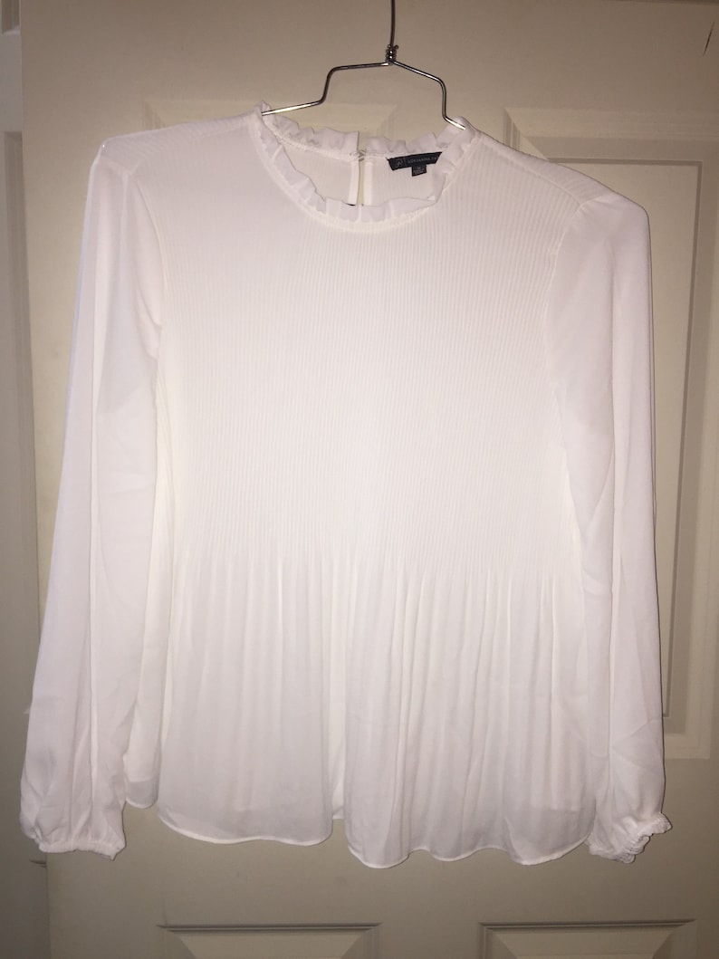 May include: White long-sleeved blouse with a ruffled collar and pleated detailing.