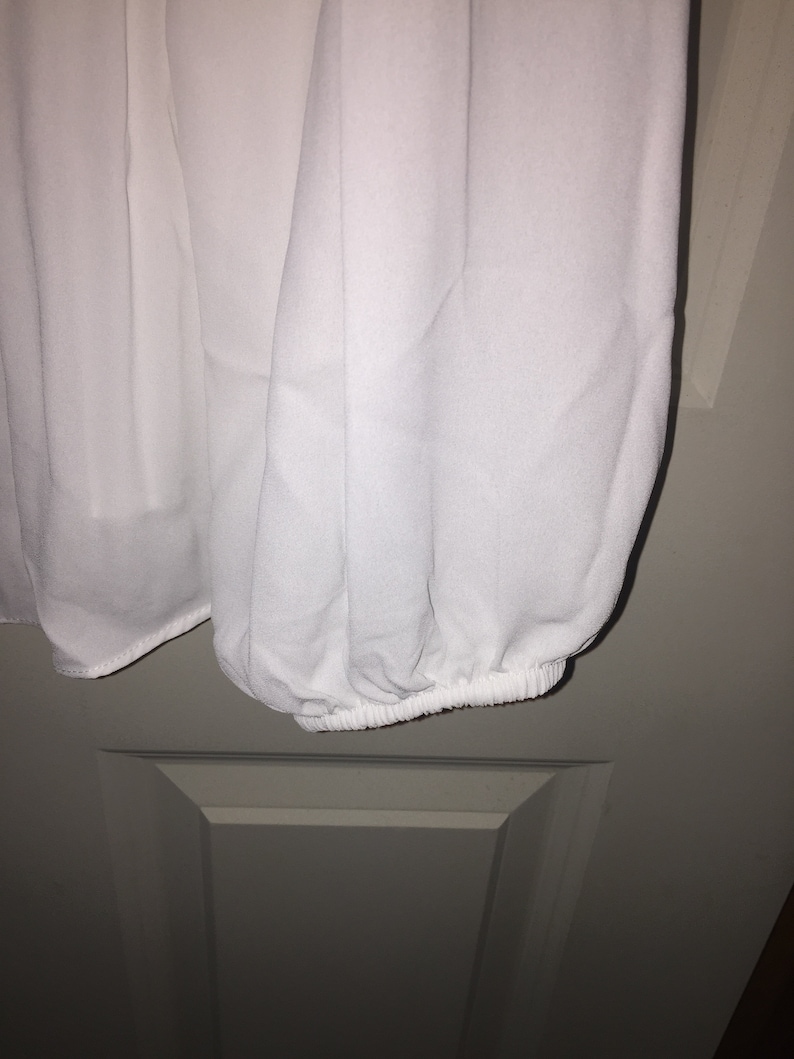 May include: White long-sleeved blouse with a gathered elastic cuff at the wrist.