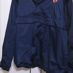 May include: Navy blue pullover windbreaker jacket with a drawstring hem. Features a mesh-lined collar and a Boston Red Sox logo patch on the chest. The jacket has a half-zip closure and long sleeves.